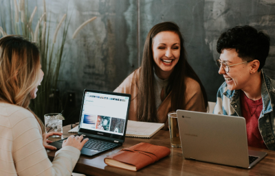 A group of women collaborating with their laptops open together at a table laughing